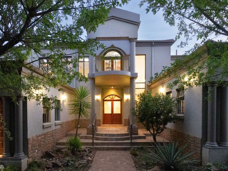 A grand double-storey residential facade featuring stone cladding, elegant columns, a central balcony, and a welcoming paved entrance.