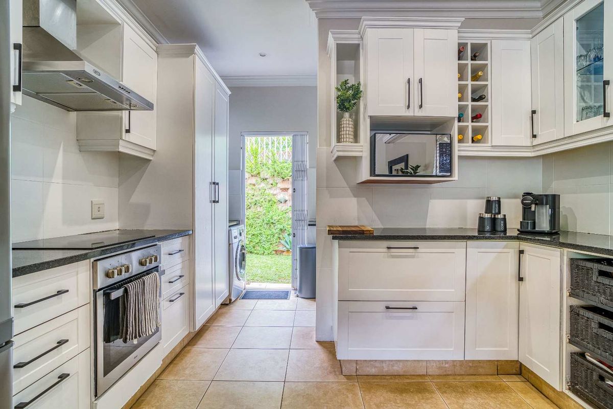 Modern kitchen featuring white cabinetry, dark stone countertops, built-in oven, extractor fan, and wine rack, leading to a rear laundry area and garden access.