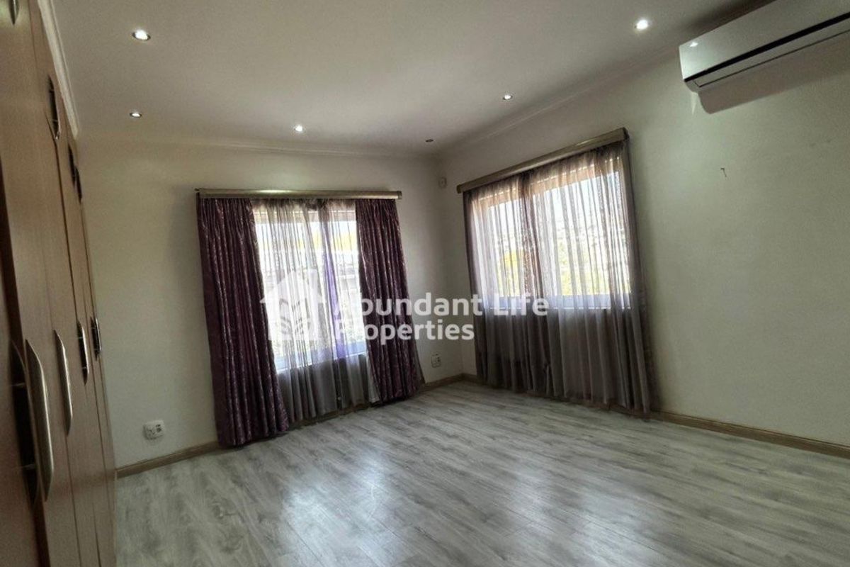 Spacious bedroom featuring light-toned laminate flooring, built-in cupboards, recessed downlighting, and a wall-mounted air conditioning unit.