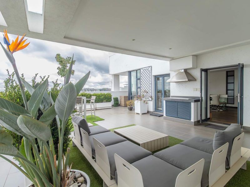 Spacious covered penthouse balcony featuring a built-in braai, stainless steel extractor, and tiled flooring, perfect for outdoor entertaining with seamless indoor-outdoor flow.