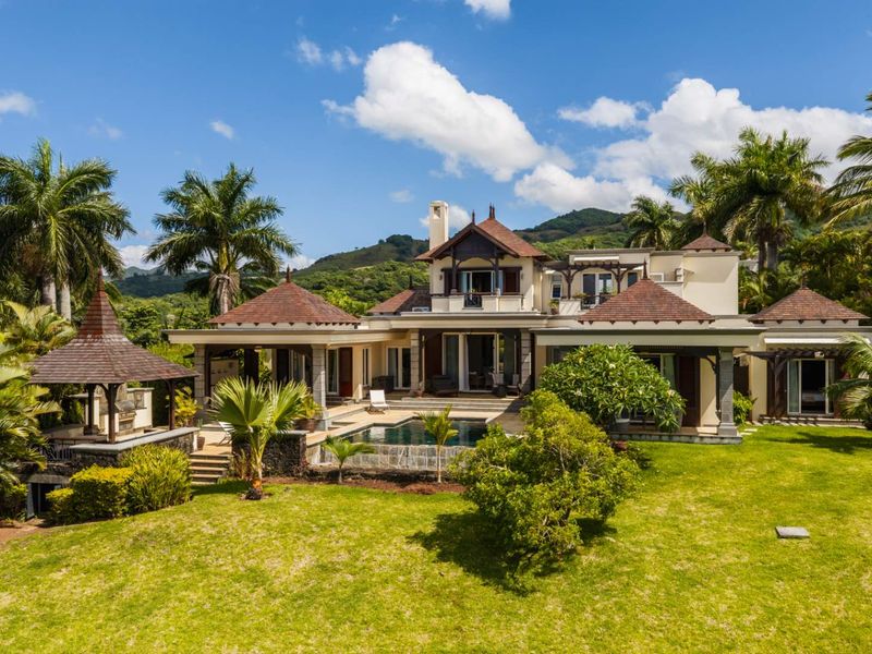 A stunning rear exterior view of a luxury villa featuring a private swimming pool, landscaped garden, and a covered gazebo area.