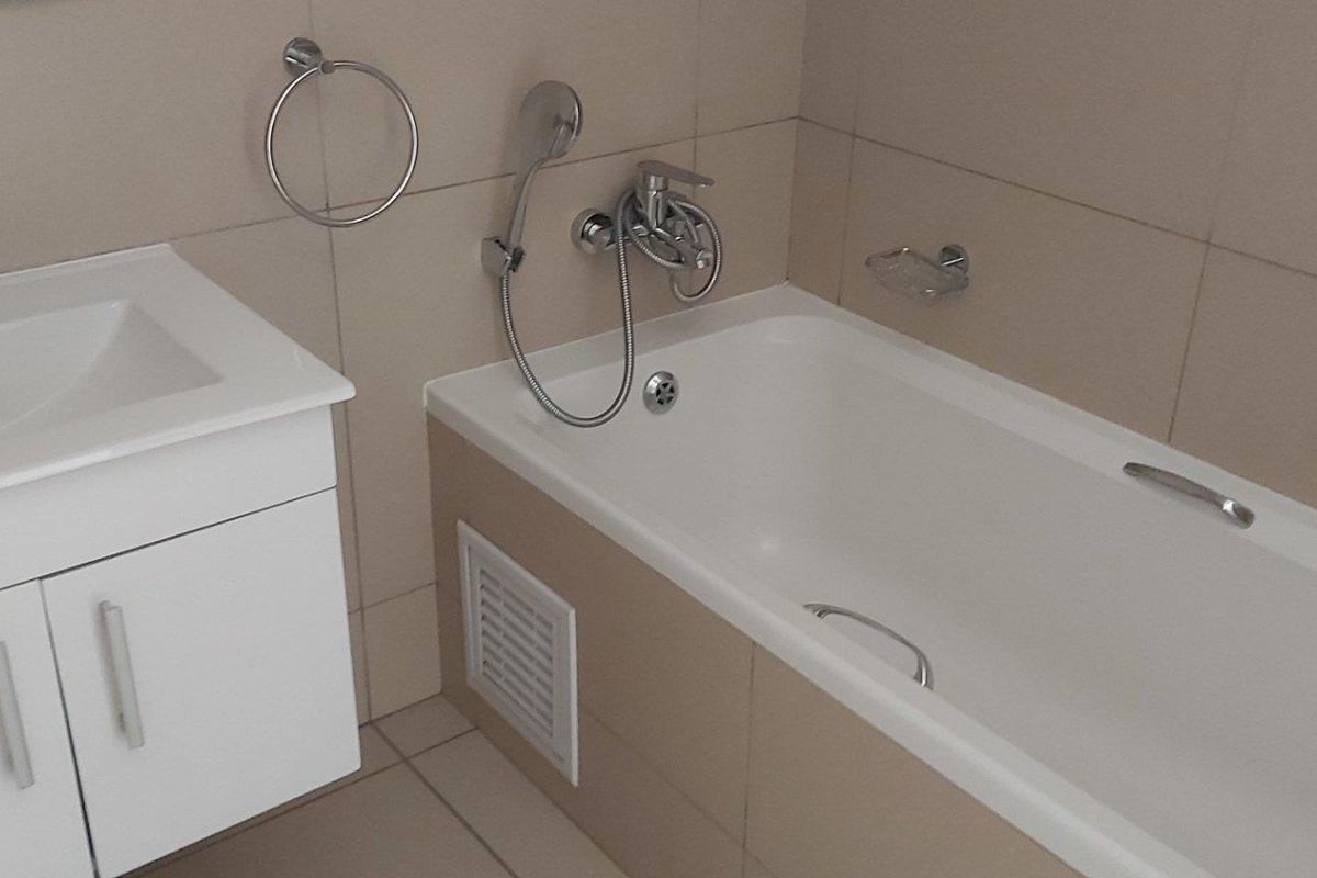 A clean, functional bathroom featuring a white vanity cabinet with basin, a bathtub with handheld shower attachment, and neutral wall tiling.