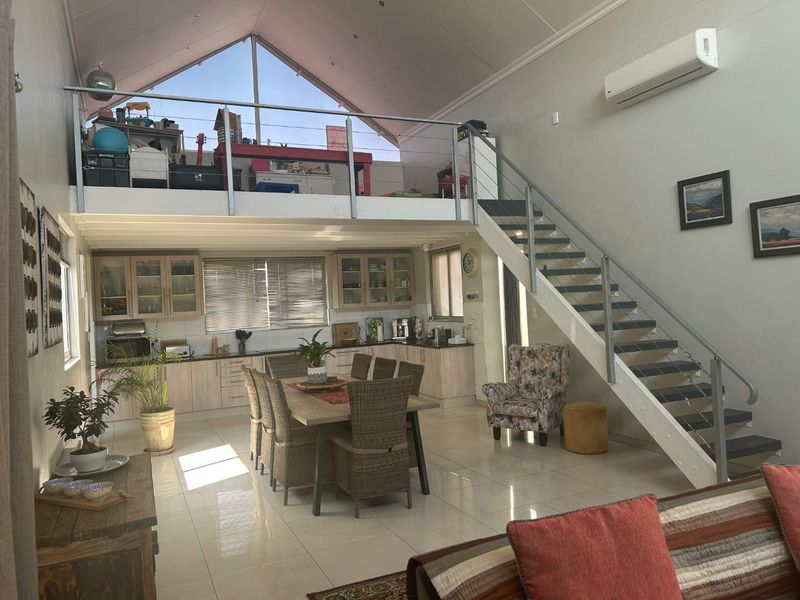 Spacious open-plan living area featuring a modern kitchen, tiled floors, a mezzanine level, and a staircase with a glass balustrade.