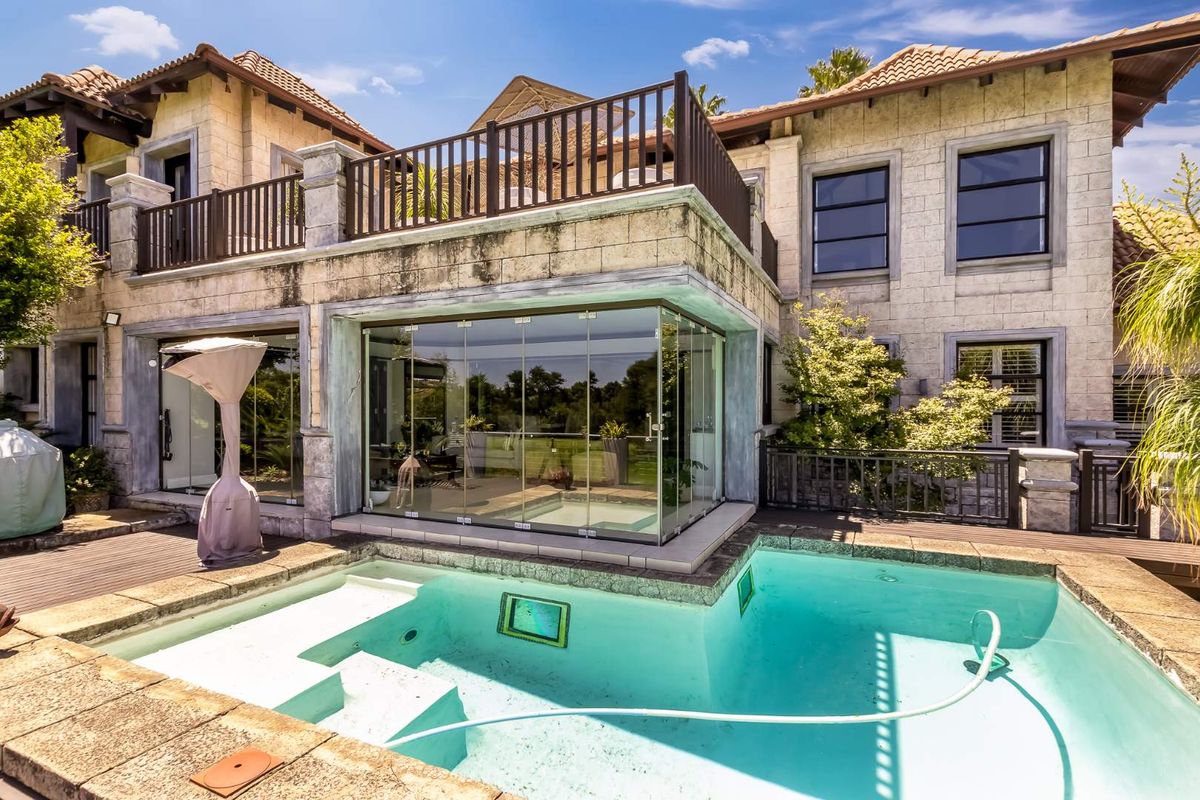 Rear view of a multi-story residence featuring a swimming pool, glass-enclosed sunroom, and an upper-level balcony with metal railings.