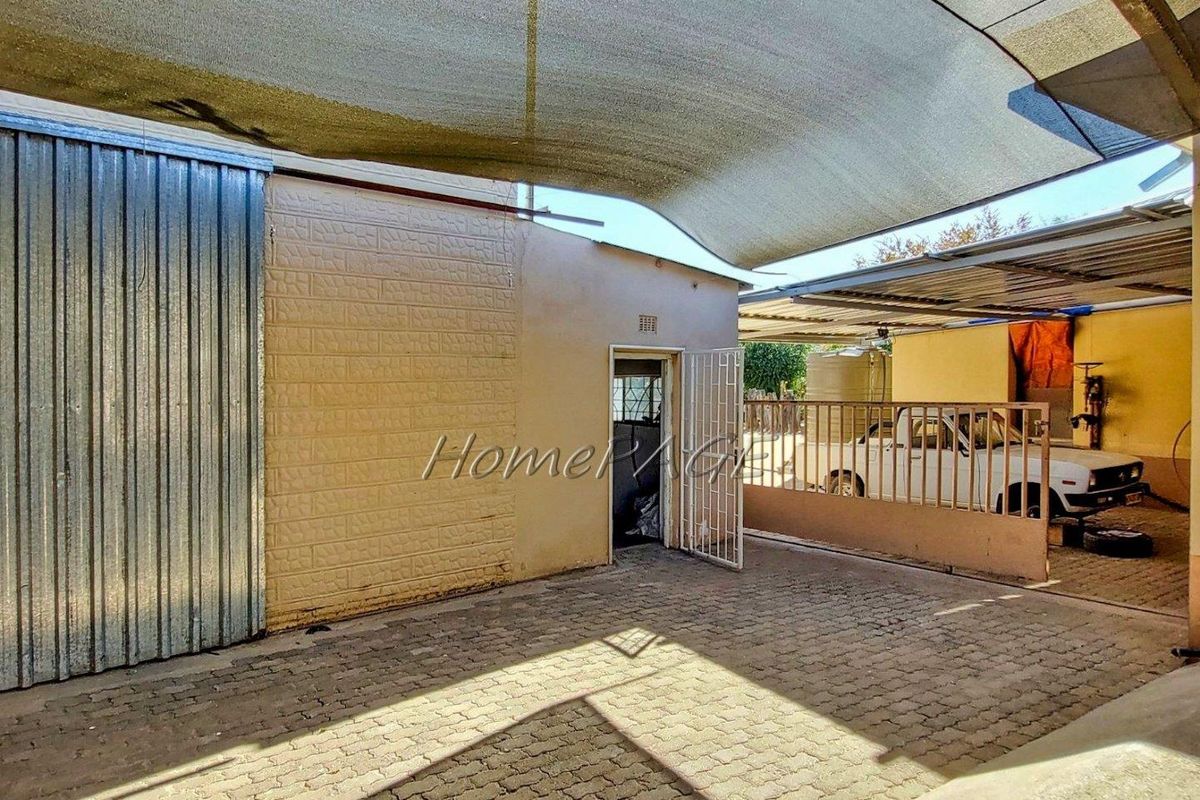 An outdoor paved courtyard area featuring a shade cloth canopy, metal security gate, and corrugated metal wall cladding.