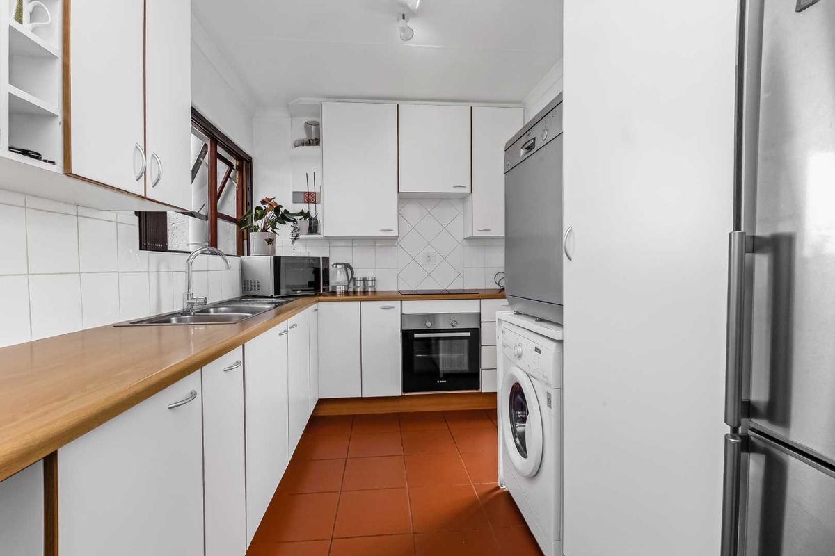 A functional kitchen featuring white cabinetry, timber-look countertops, tiled splashbacks, and integrated oven and hob, with terracotta floor tiles.