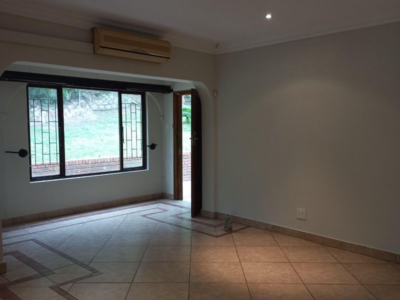 An empty living room featuring tiled flooring, recessed downlights, an integrated air conditioning unit, and an archway leading to an exterior entrance.