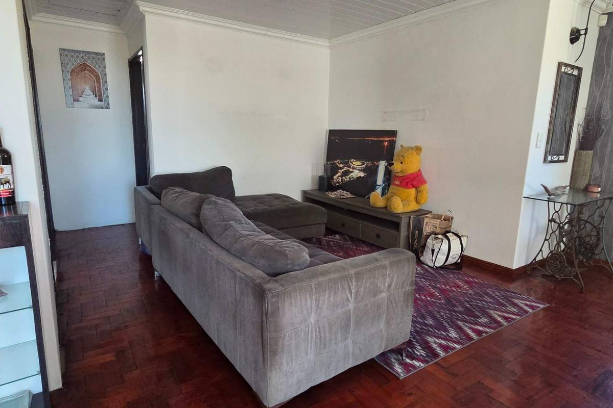 A living room featuring dark parquet flooring, coved ceilings, and a textured feature wall, providing a functional space for relaxation.