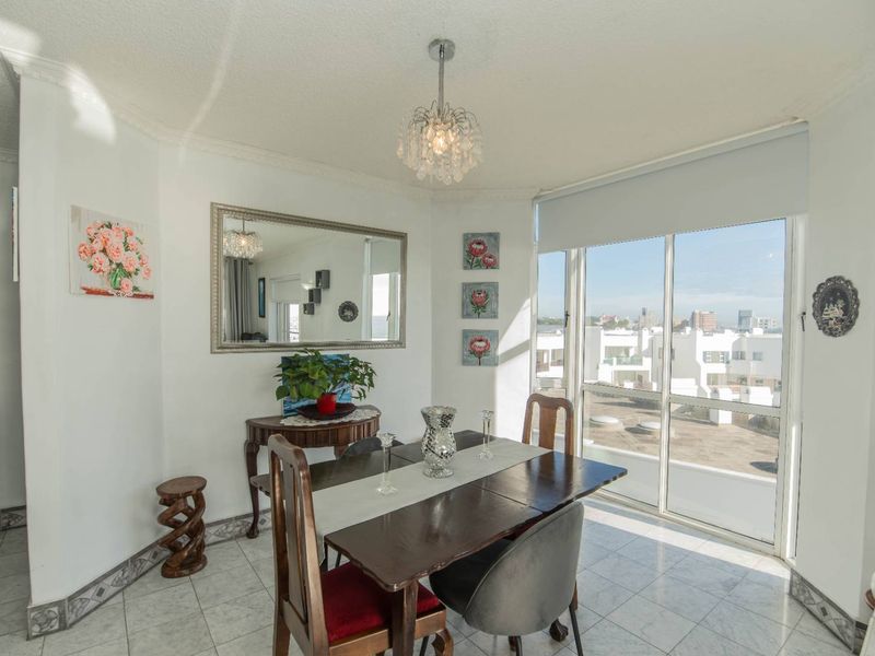 A bright dining area featuring tiled flooring, a decorative ceiling cornice, and large sliding glass doors that provide natural light and urban views.