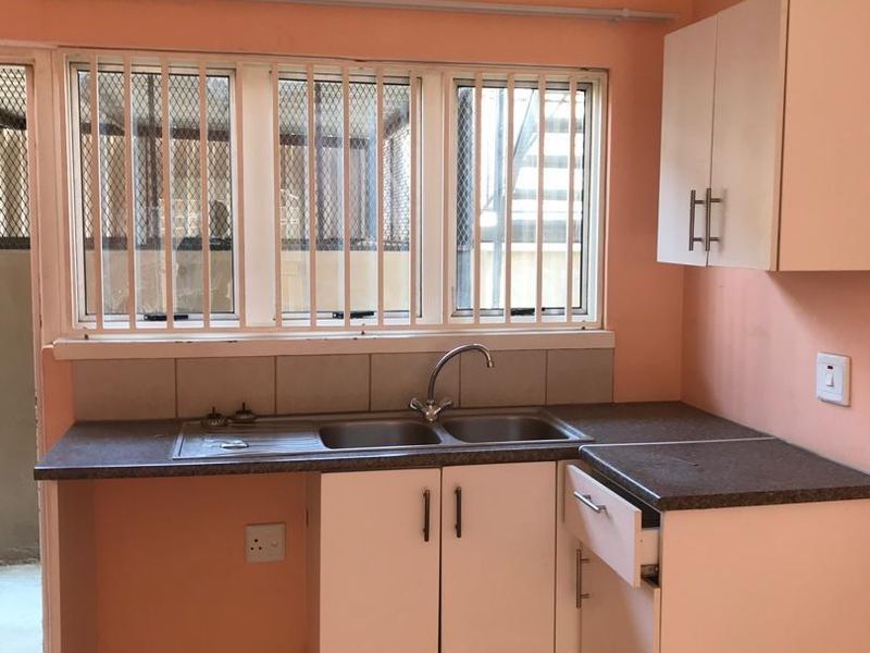 A compact kitchen featuring white cabinetry, laminate countertops, a stainless steel sink, and tiled flooring, requiring minor repairs and cosmetic updates.