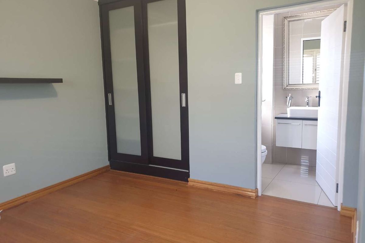 A clean, empty bedroom featuring laminate flooring, built-in sliding door wardrobes, and direct access to an en-suite bathroom.