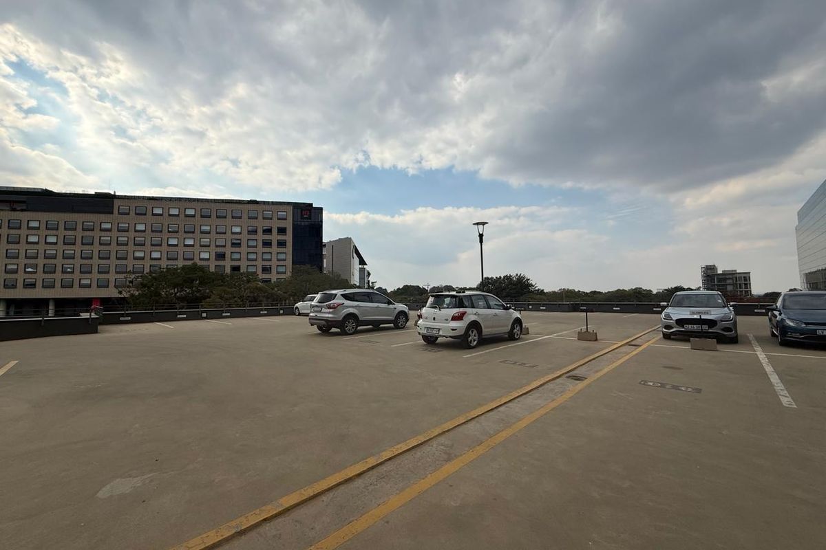 An open-air rooftop parking area featuring marked parking bays and views of surrounding office buildings.