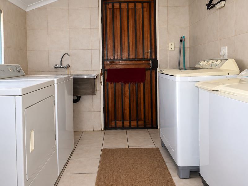 Functional laundry room featuring tiled walls and flooring, a stainless steel utility sink, and a secure exterior door.