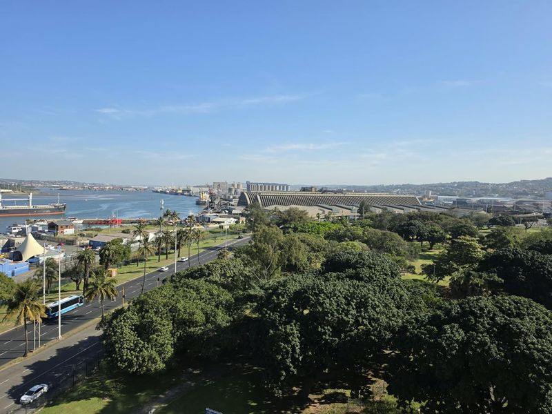 Elevated panoramic view overlooking the harbour, industrial port facilities, coastal greenery, and surrounding urban landscape.