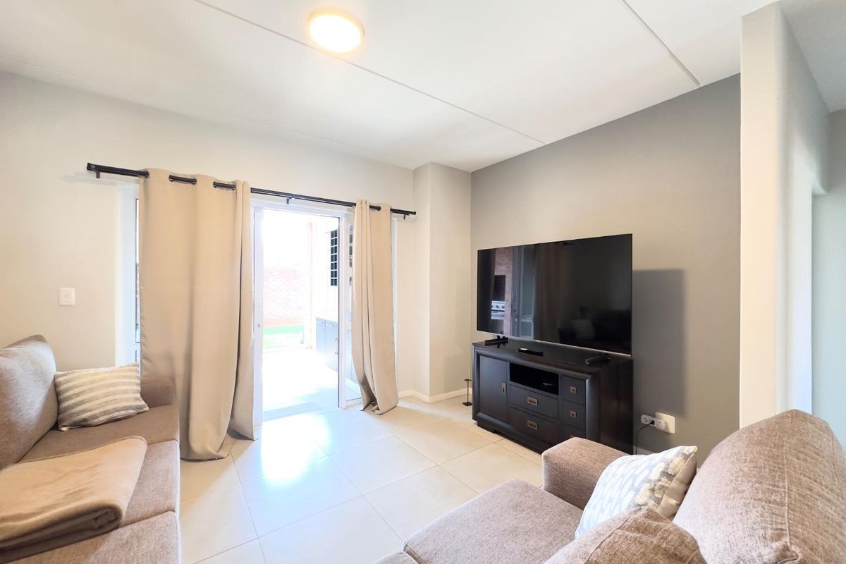 A well-maintained living room featuring neutral tiled flooring and a sliding glass door providing direct access to the outdoor area.