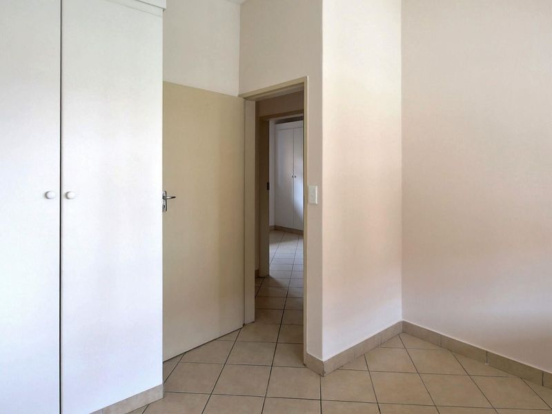 A clean, empty hallway featuring neutral tiled flooring and built-in storage cupboards, providing a functional transition space within the apartment.