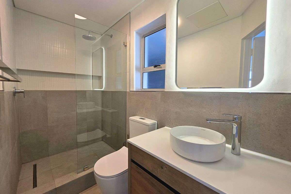 Modern bathroom featuring a walk-in shower with glass screen, vessel sink on a vanity cabinet, and an LED backlit mirror.