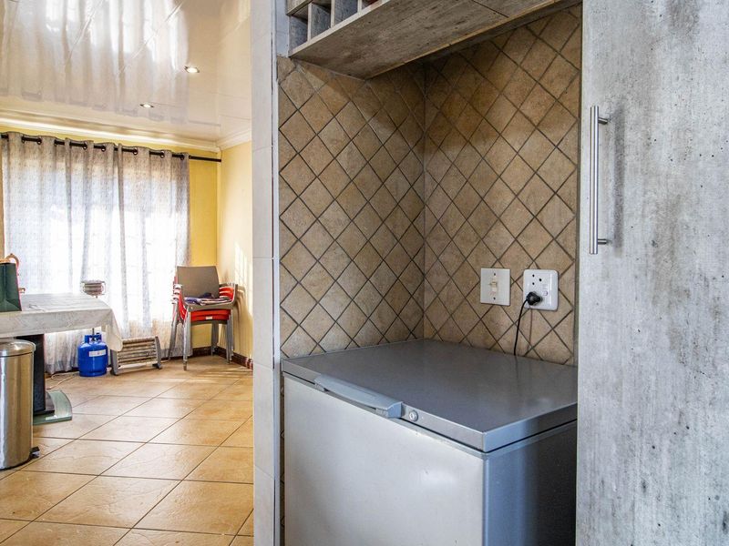 A functional utility nook featuring tiled splashbacks and electrical points, adjacent to an open-plan living and dining area with tiled flooring.