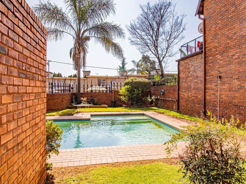 Private outdoor pool area featuring brick paving, established garden landscaping, and secure perimeter brick walling.