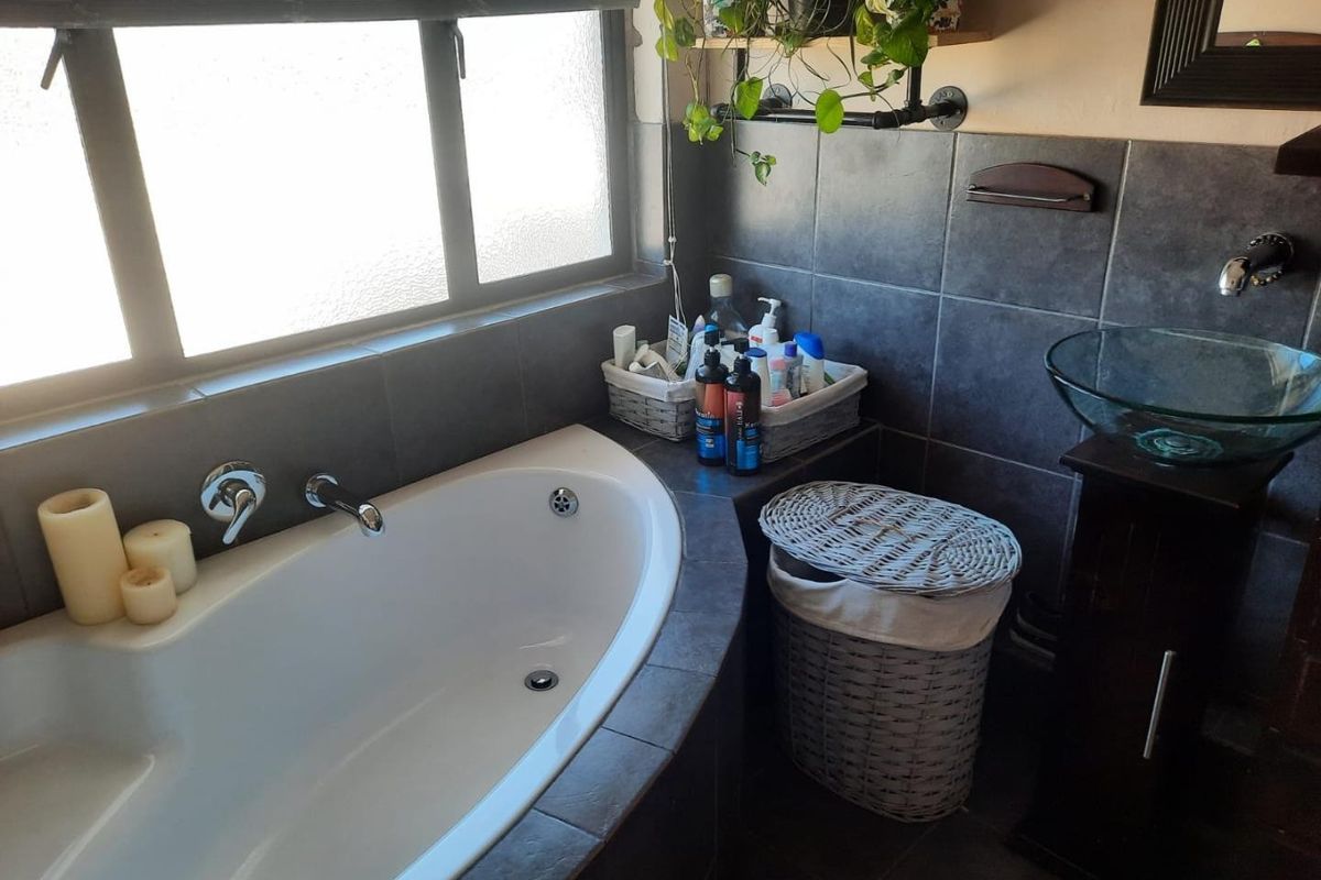 A bathroom featuring a built-in bathtub with dark tile surround, a modern vessel sink, and a window providing natural light.