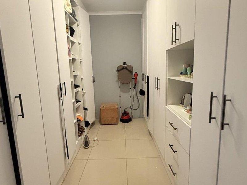 A well-organized walk-in closet featuring extensive white built-in cabinetry, ample shelving, and clean tiled flooring.