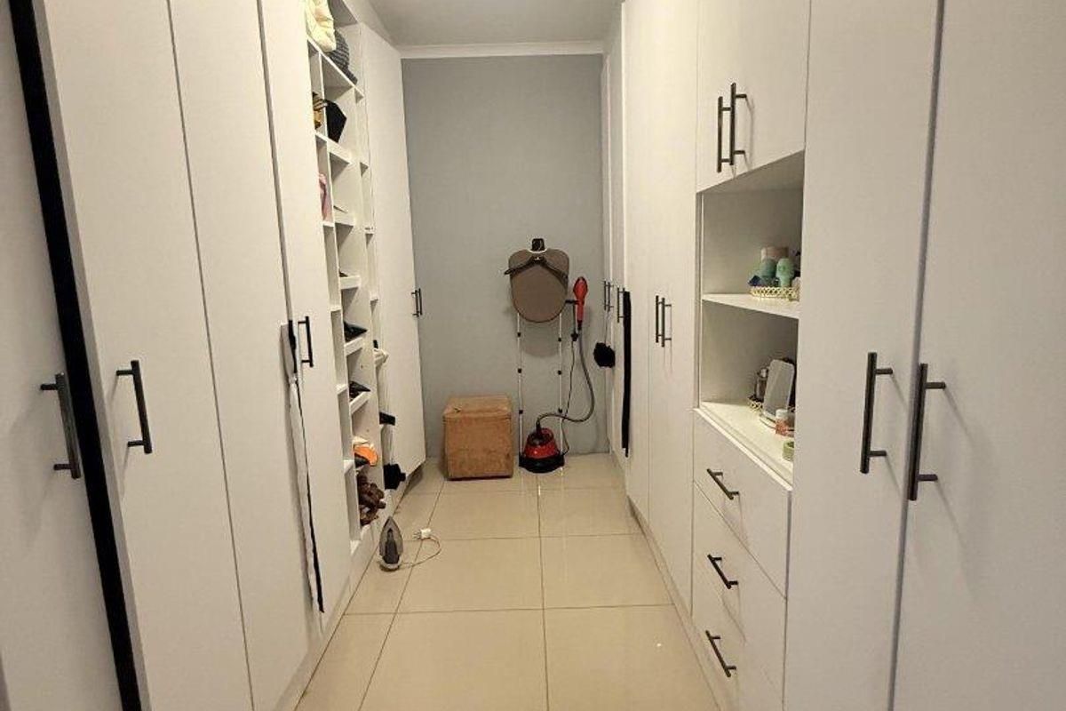 A well-organized walk-in closet featuring extensive white built-in cabinetry, ample shelving, and clean tiled flooring.