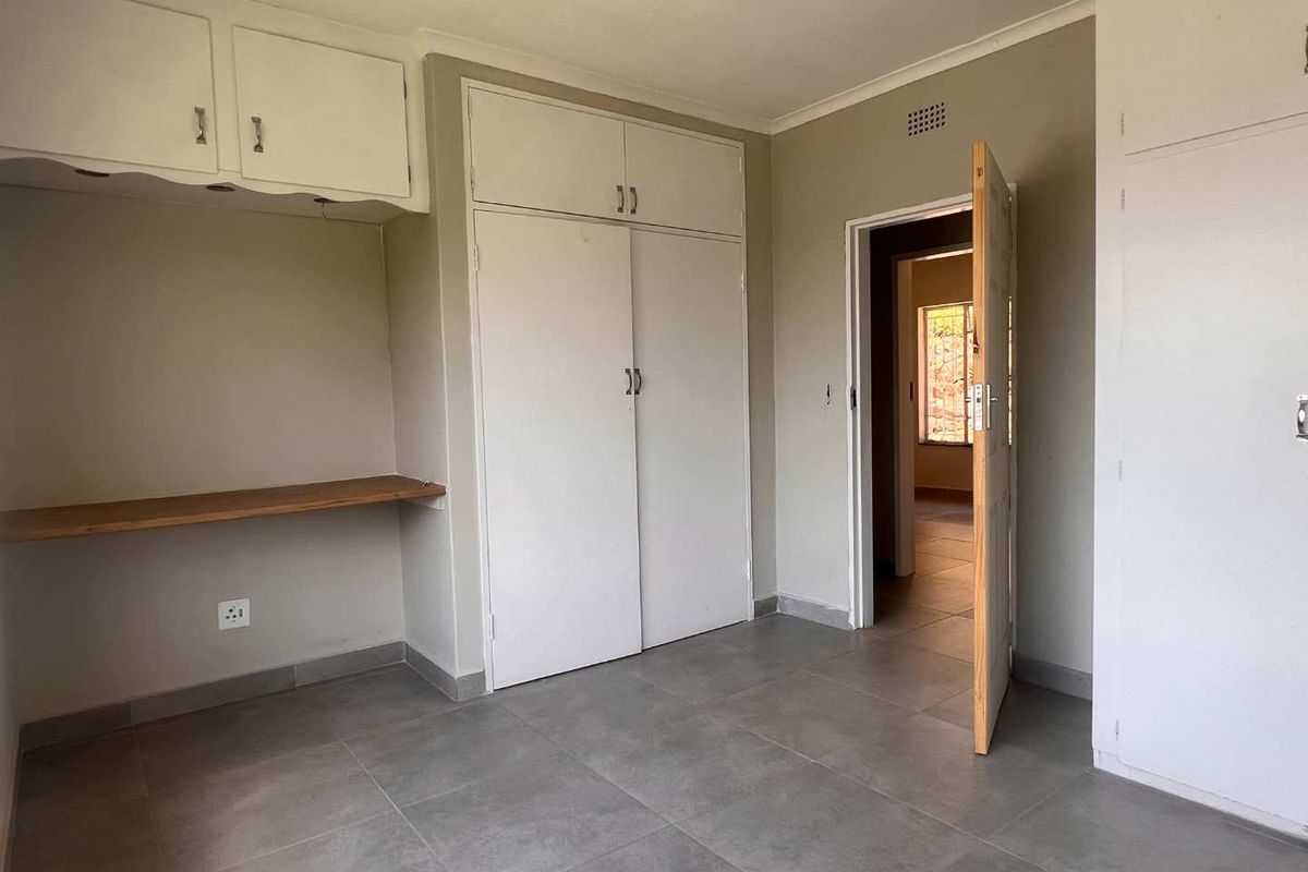 A vacant bedroom featuring neutral tiled flooring, built-in cupboards with overhead storage, and a built-in desk area.