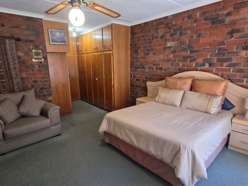 Spacious bedroom featuring exposed brick walls, fitted wooden built-in cupboards, and a ceiling fan.