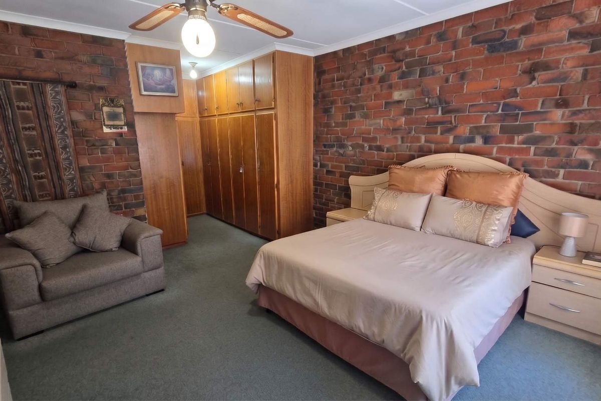 Spacious bedroom featuring exposed brick walls, fitted wooden built-in cupboards, and a ceiling fan.