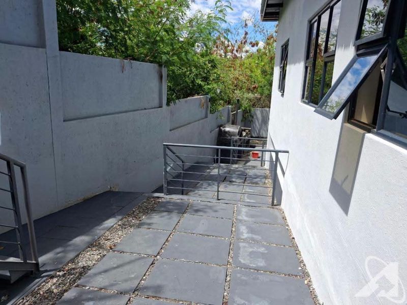 A paved exterior walkway along the side of the building featuring concrete boundary walls and metal safety railings.