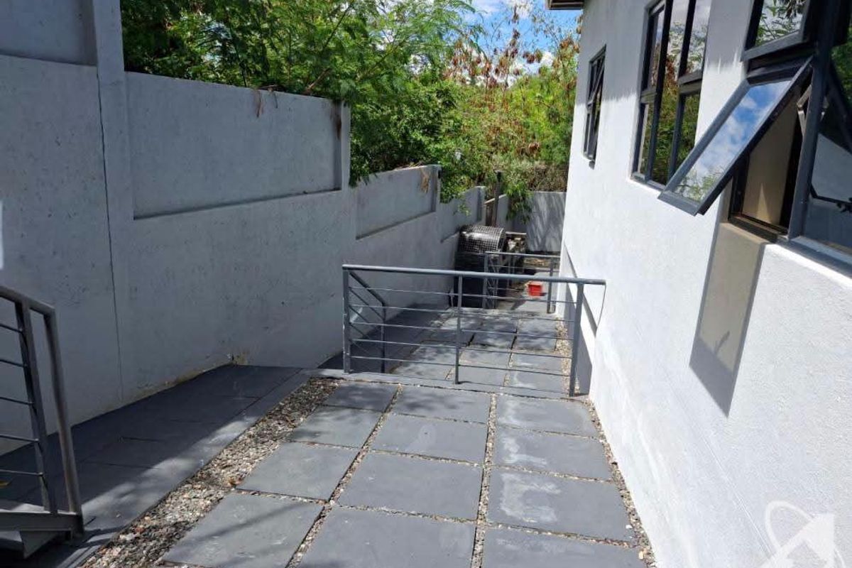 A paved exterior walkway along the side of the building featuring concrete boundary walls and metal safety railings.