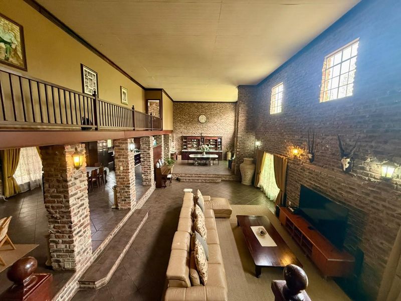 Spacious open-plan living area featuring double-volume exposed brick walls, a mezzanine level with timber balustrade, and a raised dining platform.