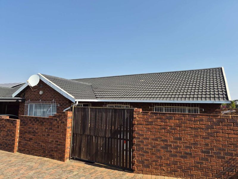 Front exterior view of a face brick townhouse featuring a tiled roof, security bars on windows, and a private timber gate entrance.