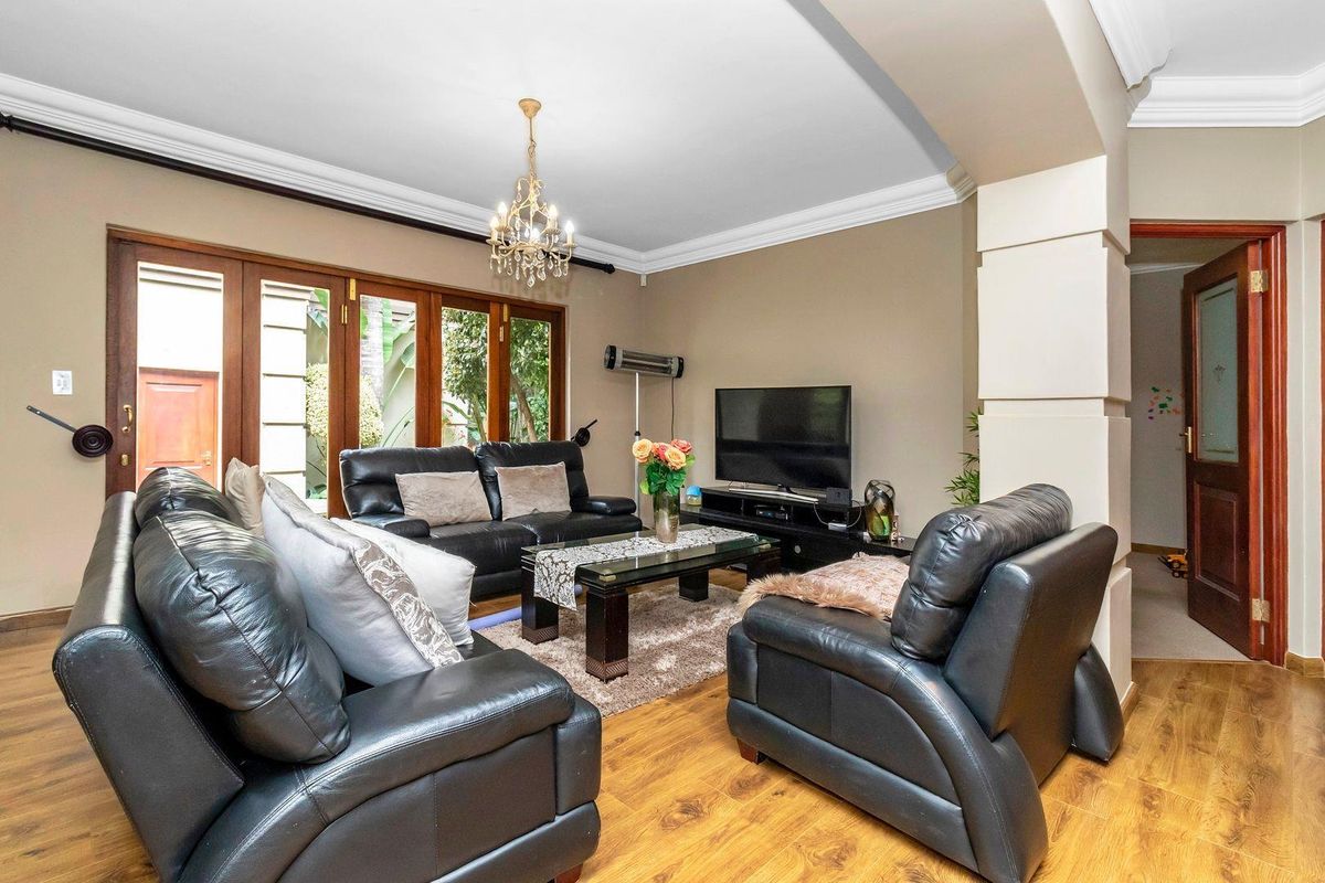 A comfortable living room featuring wooden flooring, decorative ceiling cornices, and large wooden-framed glass doors providing access to the outdoor area.