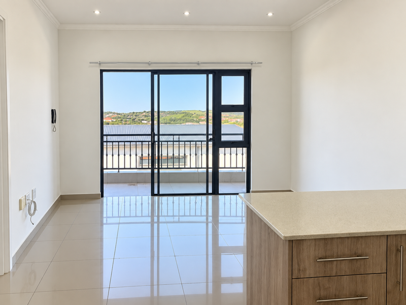 Bright open-plan living area featuring modern tiled floors, recessed lighting, and a large sliding door leading to a balcony with scenic views.