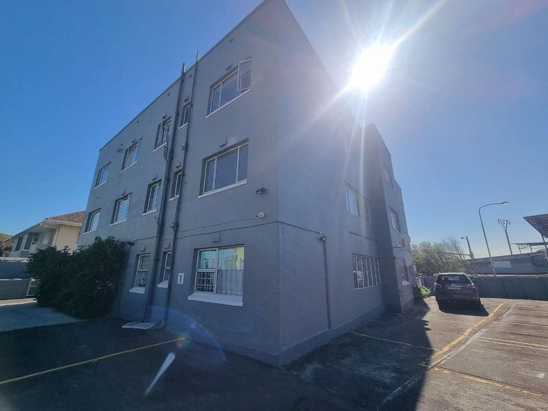 Exterior view of a multi-story apartment building featuring a painted masonry facade, aluminium window frames, and an adjacent asphalt parking area.