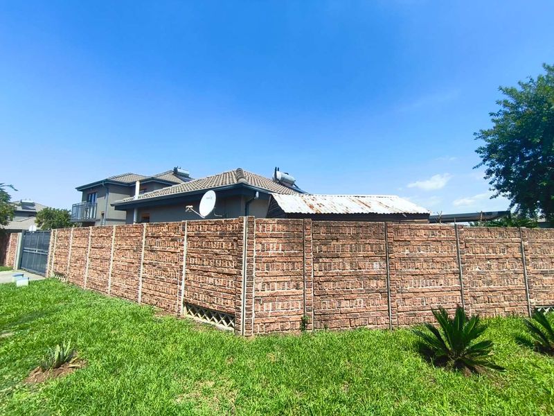 Rear view of the property featuring a precast concrete boundary wall, a lawn area, and a structure with a weathered corrugated metal roof.