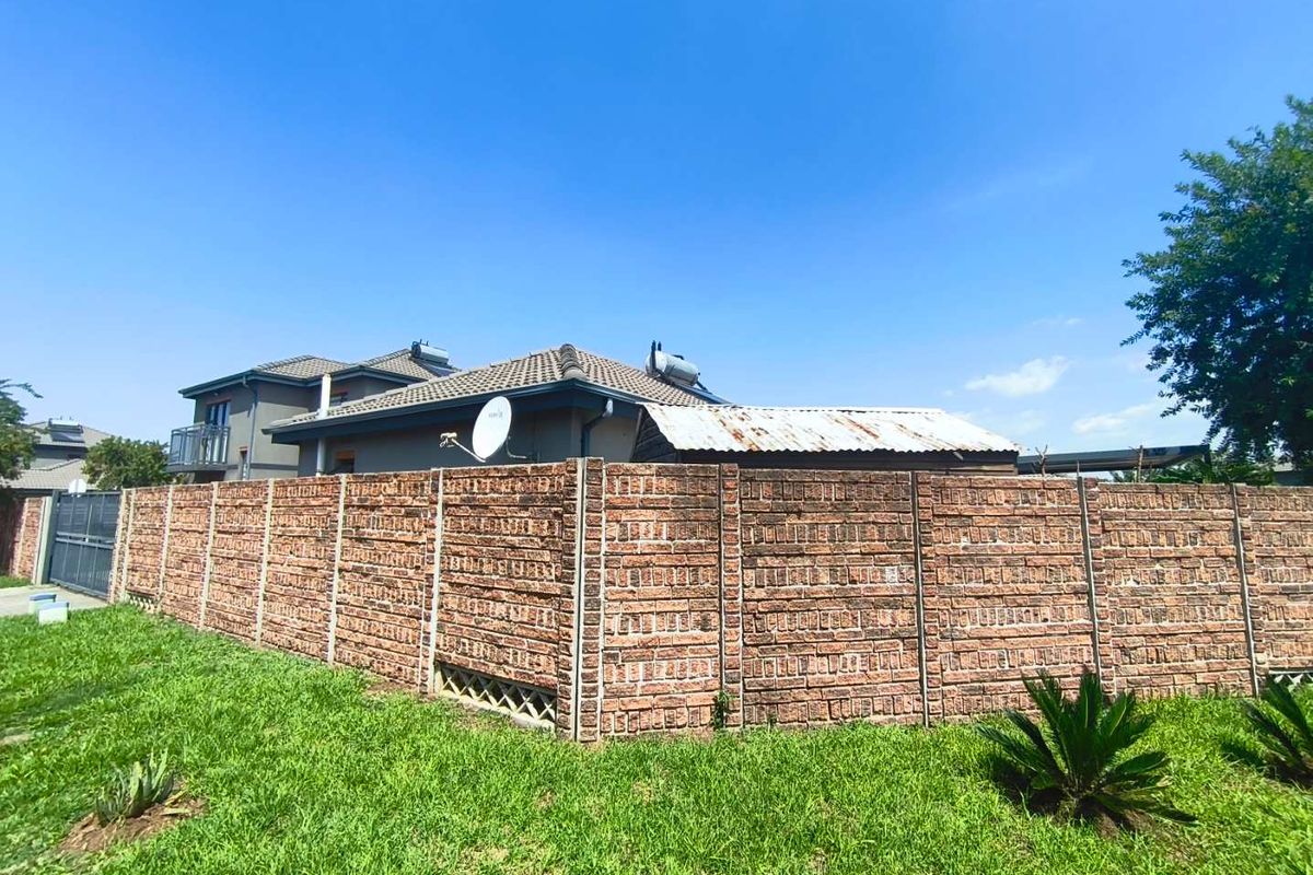 Rear view of the property featuring a precast concrete boundary wall, a lawn area, and a structure with a weathered corrugated metal roof.