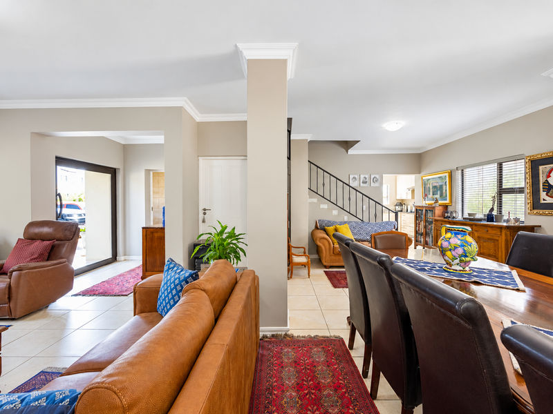Spacious open-plan living and dining area featuring tiled flooring, crown molding, and a staircase, with direct access to the exterior through a sliding door.
