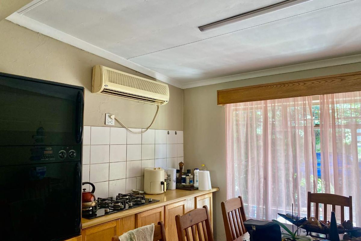 A functional kitchen area featuring wooden cabinetry, a built-in gas hob, and an integrated oven, complemented by a wall-mounted air conditioning unit.