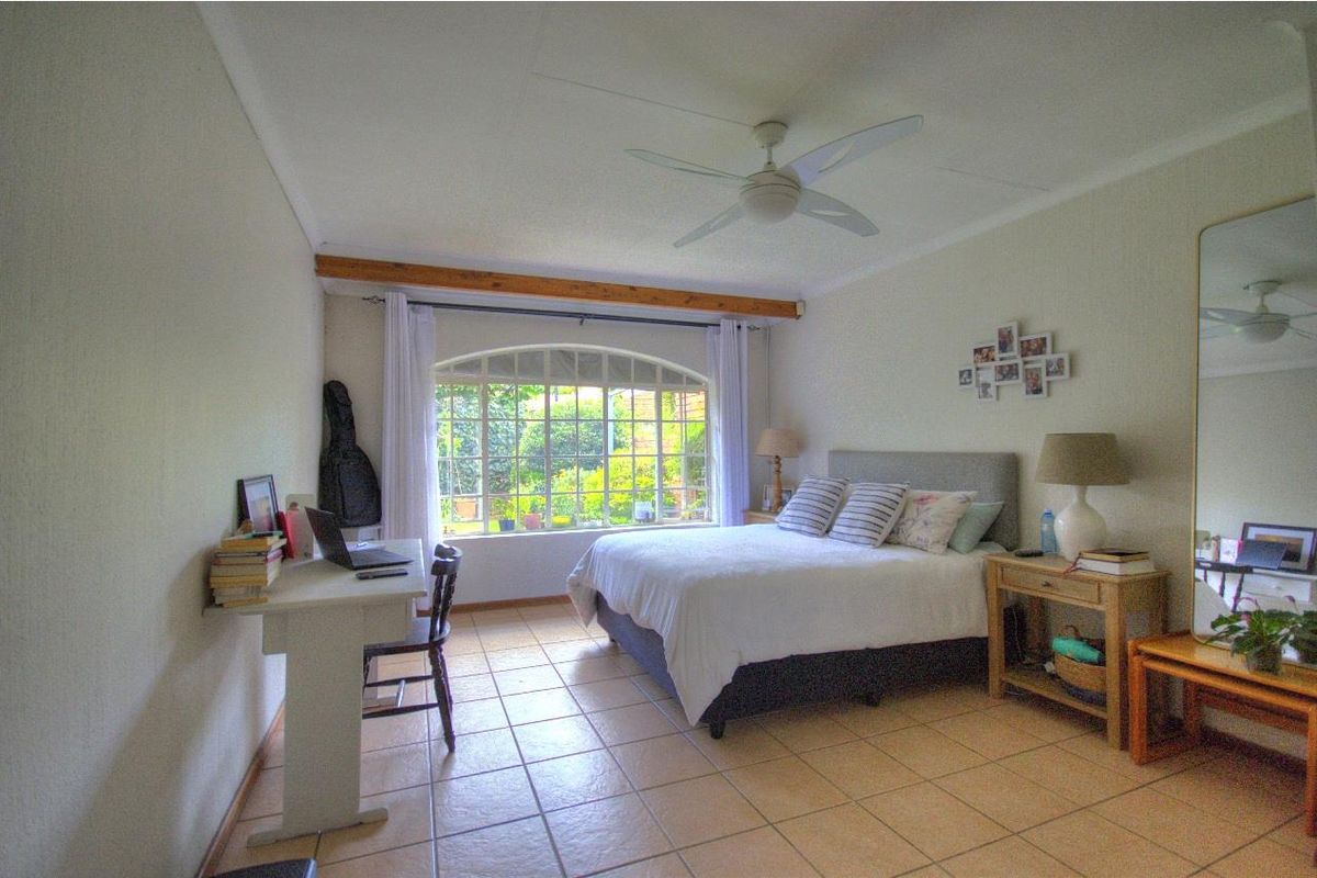 A well-lit bedroom featuring tiled flooring, a ceiling fan, and a large arched window overlooking the garden.