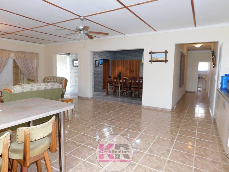 Spacious open-plan living and dining area featuring tiled flooring, a ceiling fan, and exposed beam ceiling details, connecting to adjacent living spaces.