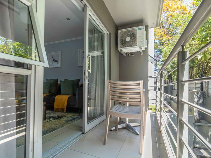 A private balcony featuring tiled flooring, a metal balustrade, and a wall-mounted air conditioning unit, providing seamless access to the interior living space.
