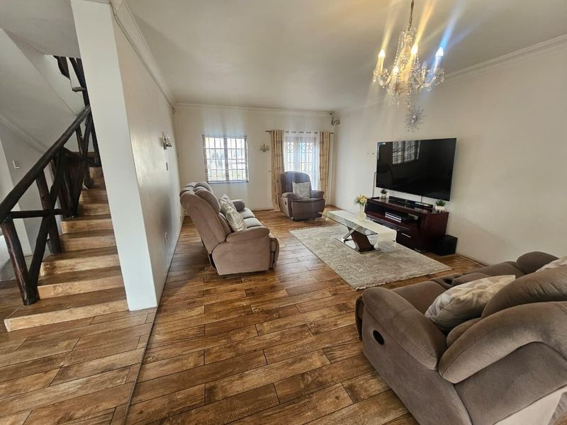 Spacious living room featuring wood-look tile flooring, a wooden staircase, and decorative chandelier lighting, creating a warm and inviting atmosphere.
