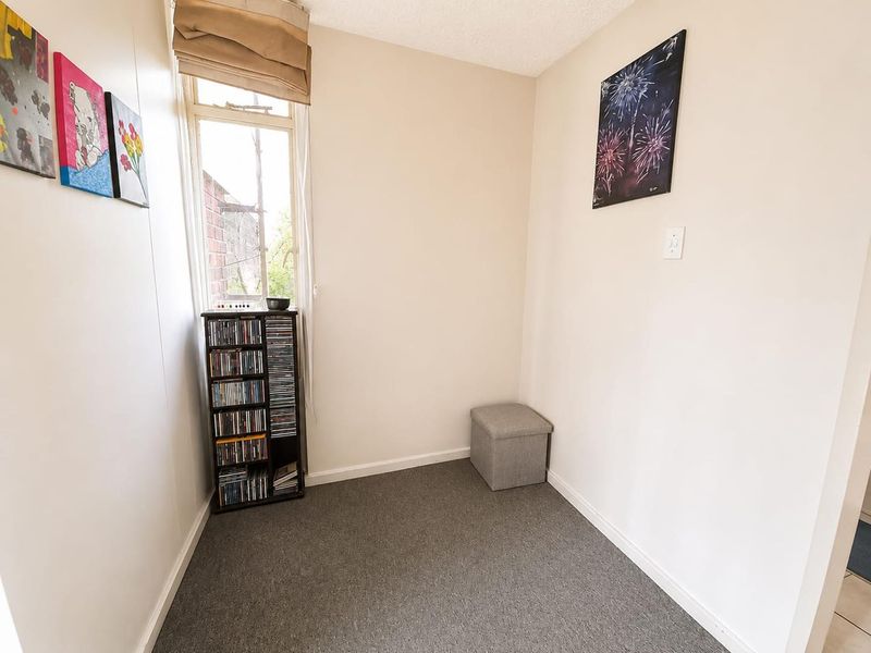 A compact bedroom featuring neutral walls, carpeted flooring, and a single window providing natural light.