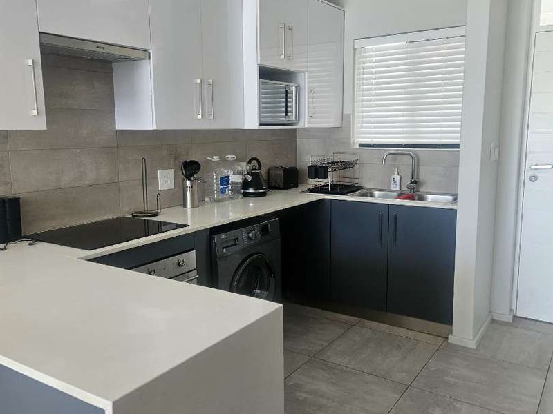 Modern kitchen featuring sleek two-tone cabinetry, stone countertops, integrated appliances, and tiled flooring with a functional layout.