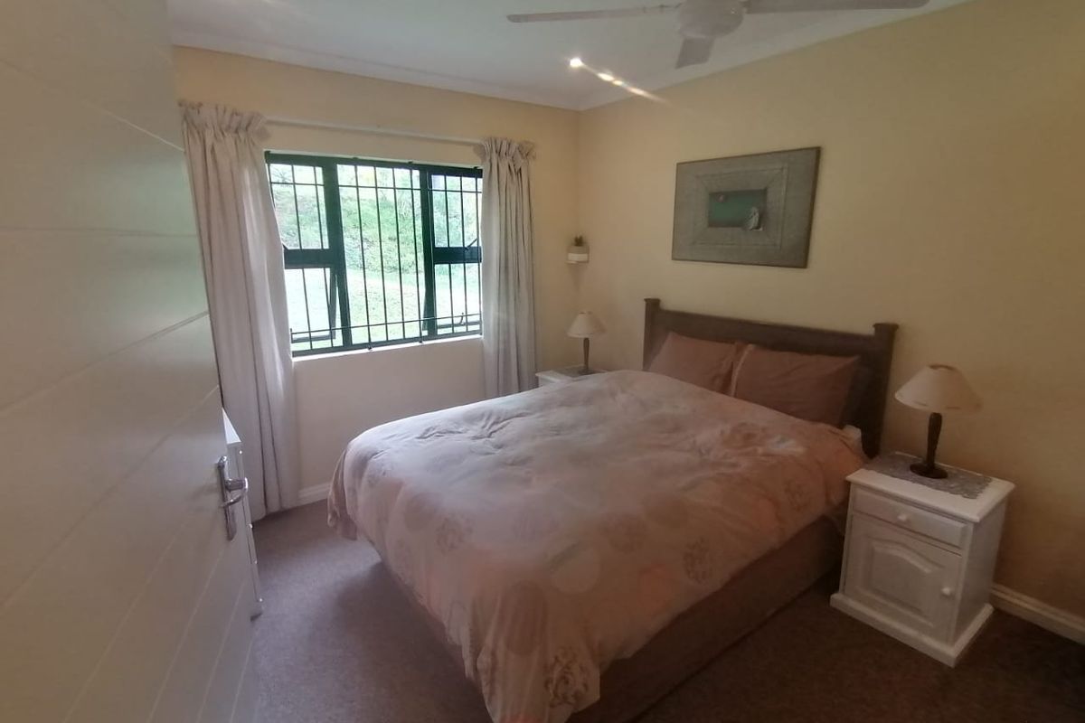A cozy bedroom featuring a ceiling fan, security bars on the window, and neutral wall finishes.