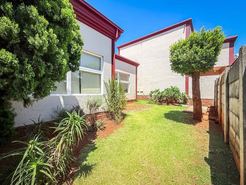 A private rear garden featuring a small paved patio area, established landscaping, and a secure brick boundary wall.