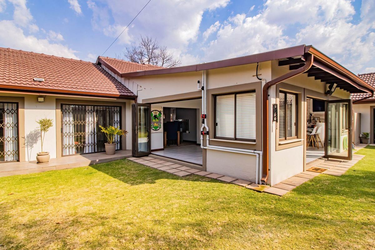 Rear view of the house featuring a well-maintained lawn, paved pathways, and bi-fold doors providing seamless indoor-outdoor flow.