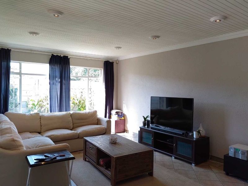 A comfortable living room featuring tiled flooring, a textured tongue and groove ceiling, and recessed downlighting, providing a bright and functional space.